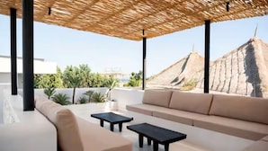 Un área de estar moderna al aire libre con techo de paja, un sofá y dos mesitas.