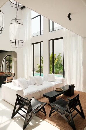 Ein modernes Wohnzimmer mit einem weißen Modulsofa, schwarzen Stühlen, einem schwarzen Couchtisch und großen Fenstern mit Blick auf einen Pool und Grünflächen.