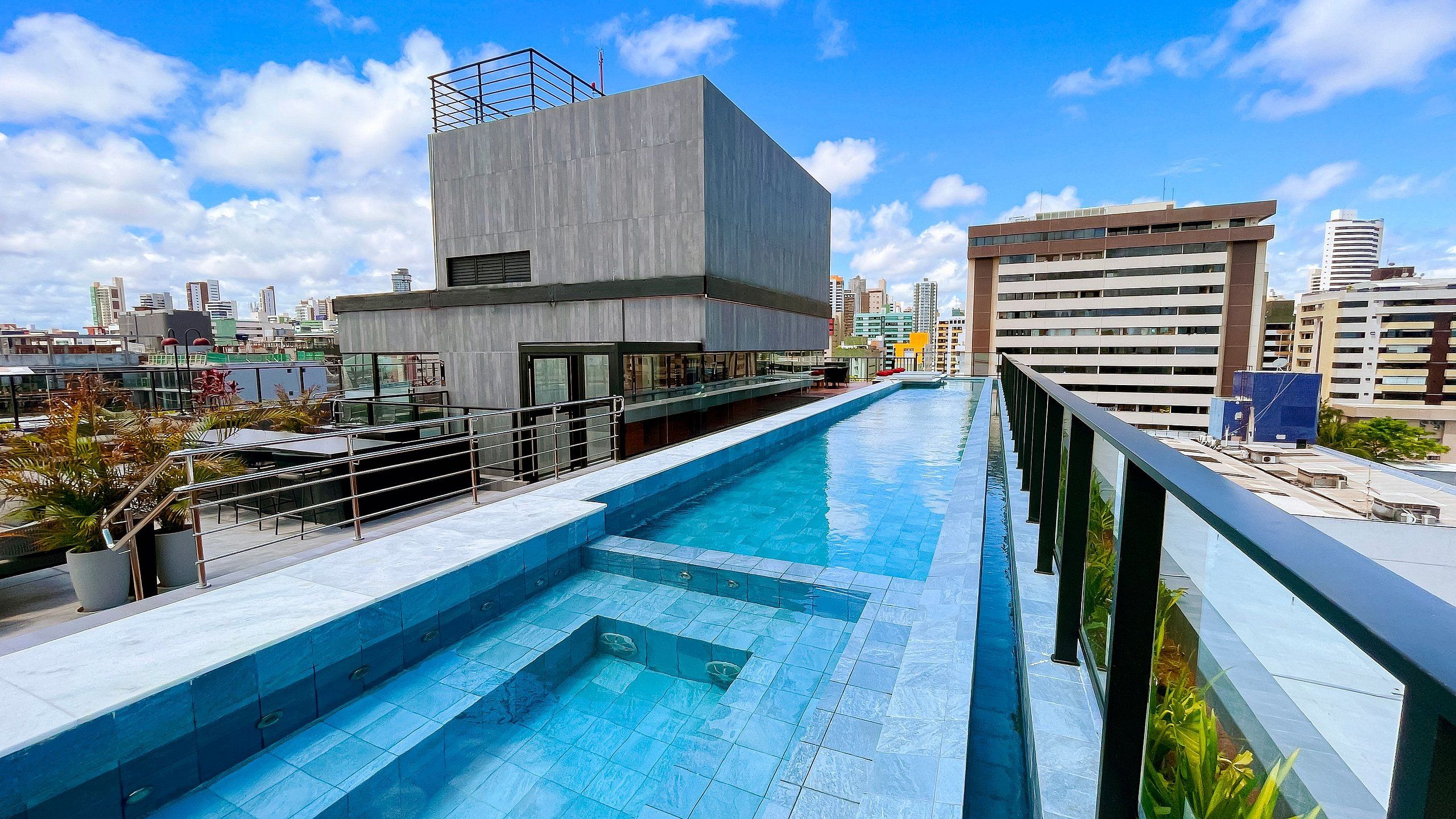 Une piscine sur le toit offrant une vue sur les gratte-ciel de la ville, un bâtiment moderne à la façade en béton et un ciel d’un bleu éclatant.