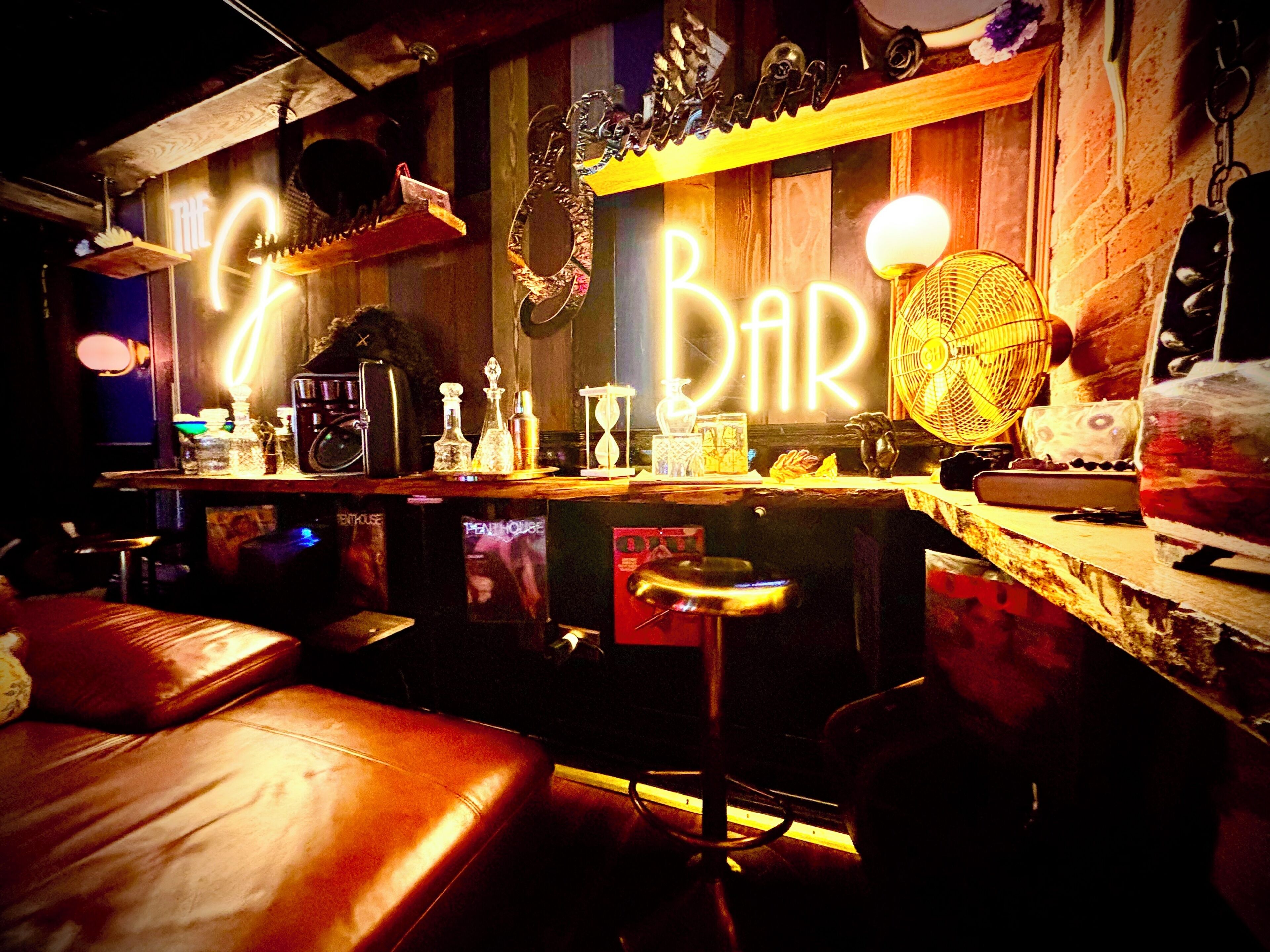 A bar with a neon sign, bar stools, and various bar accessories.
