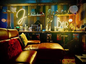 Eine Bar mit einer Neonreklame, Holzböden mit Flaschen und einer Ledersofa.