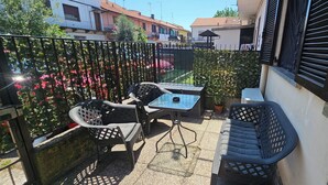 A balcony with a table and chairs, a potted plant, and a view of neighboring buildings.