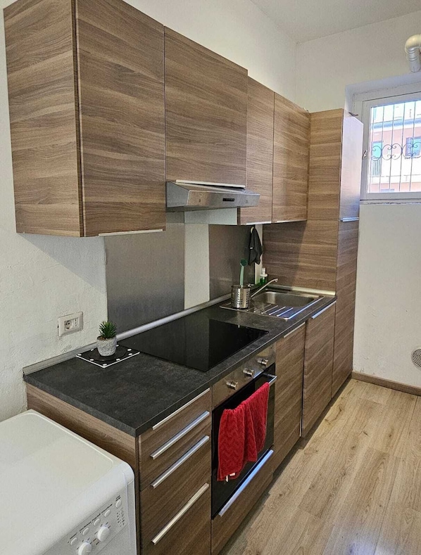 Une cuisine moderne avec des meubles en bois, un plan de travail noir, un évier en acier inoxydable et un four encastré.