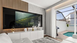 Ein modernes Wohnzimmer mit großem Flachbildfernseher, weißen Sofas, einer Wandpaneele aus Holz und Blick auf einen Swimmingpool.
