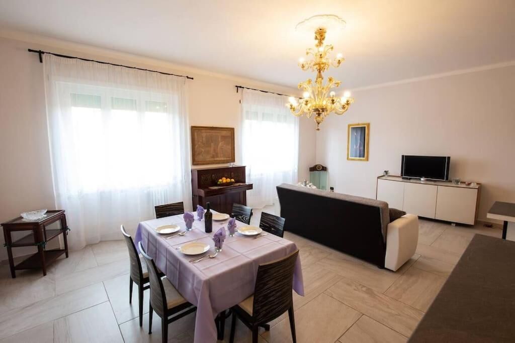Zona pranzo con tavolo apparecchiato per quattro persone, divano, televisione e lampadario.