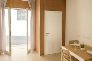 Ein modernes Zimmer mit einer Schiebetür aus Glas, einer Wandpaneele aus Holz, einer weißen Tür und einer Essecke mit Tisch, Stühlen und einem Blumentopf.