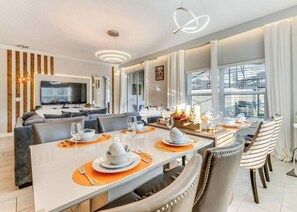 A modern hotel room with a dining area, a sofa, a TV, and a balcony with curtains. - Last Minute Disney Getaway! Private Pool & Themed Bedrooms. Book Now! #154061 (Orlando)