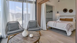 Ein modernes Hotelzimmer mit einem Bett, zwei Sesseln, einem runden Tisch und Blick auf die Stadt.