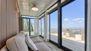 Ein modernes Wohnzimmer mit einer Couch, großen Fenstern und Blick auf eine entfernte Landschaft.