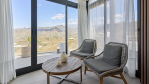 Ein Balkon mit zwei Korbstühlen, einem runden Holztisch und Blick auf eine gebirgige Landschaft.