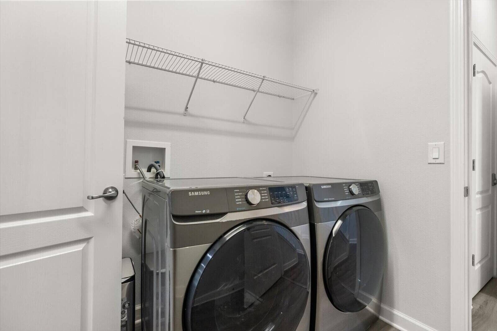 A laundry room with two Samsung washers and dryers, a metal drying rack, and a door.