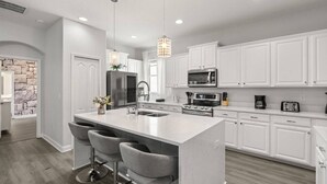 Una cocina moderna con armarios blancos, una isla central con taburetes, un refrigerador de acero inoxidable, un microondas y un horno.