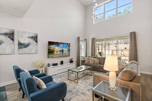 A spacious living room with a large window, a sofa set, a coffee table, and artwork on the walls. - Last Minute Disney Getaway! Luxury Villa with Private Pool. Book Now! #155727 (Orlando)