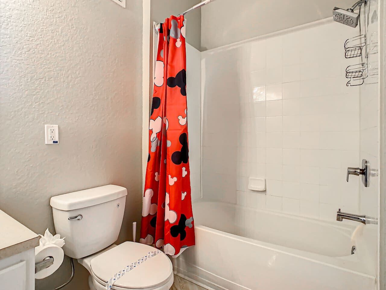 A bathroom with a toilet, shower, and a Mickey Mouse themed shower curtain.