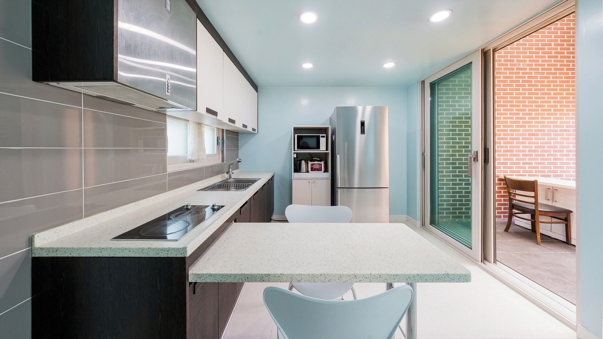 A compact kitchen with a built-in stove, microwave, and refrigerator, a dining area with a table and chairs, and a sliding glass door leading to a brick wall.