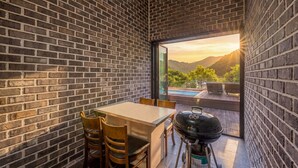 A patio with a table and chairs, a grill, and a view of mountains through a glass door. - Gapyeong Valley Scoop Pension (Gapyeong)