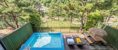 A rooftop pool with a view of a forested area, a wooden deck, and lounge chairs.