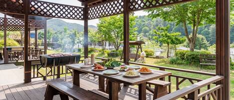 An outdoor dining area with a grill, wooden tables, and benches.