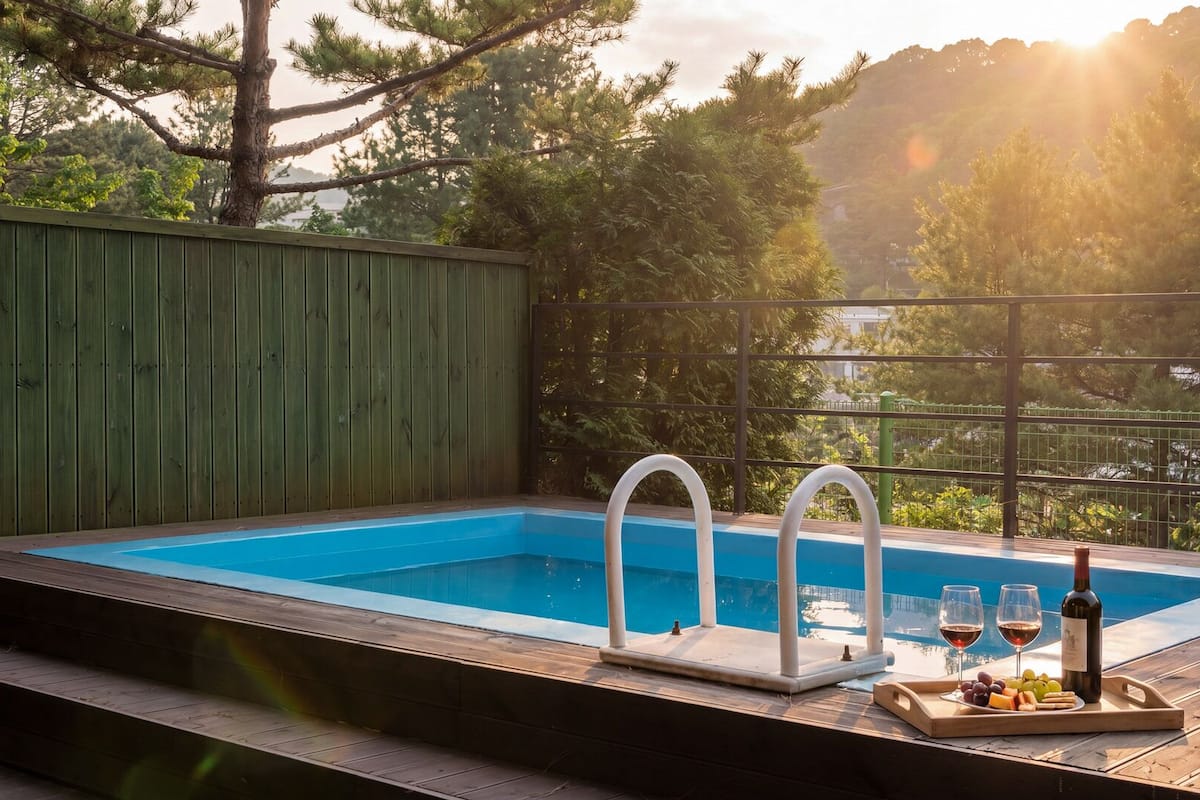 En swimmingpool med træterrasse, metalhegn og udsigt til træer og bakker.