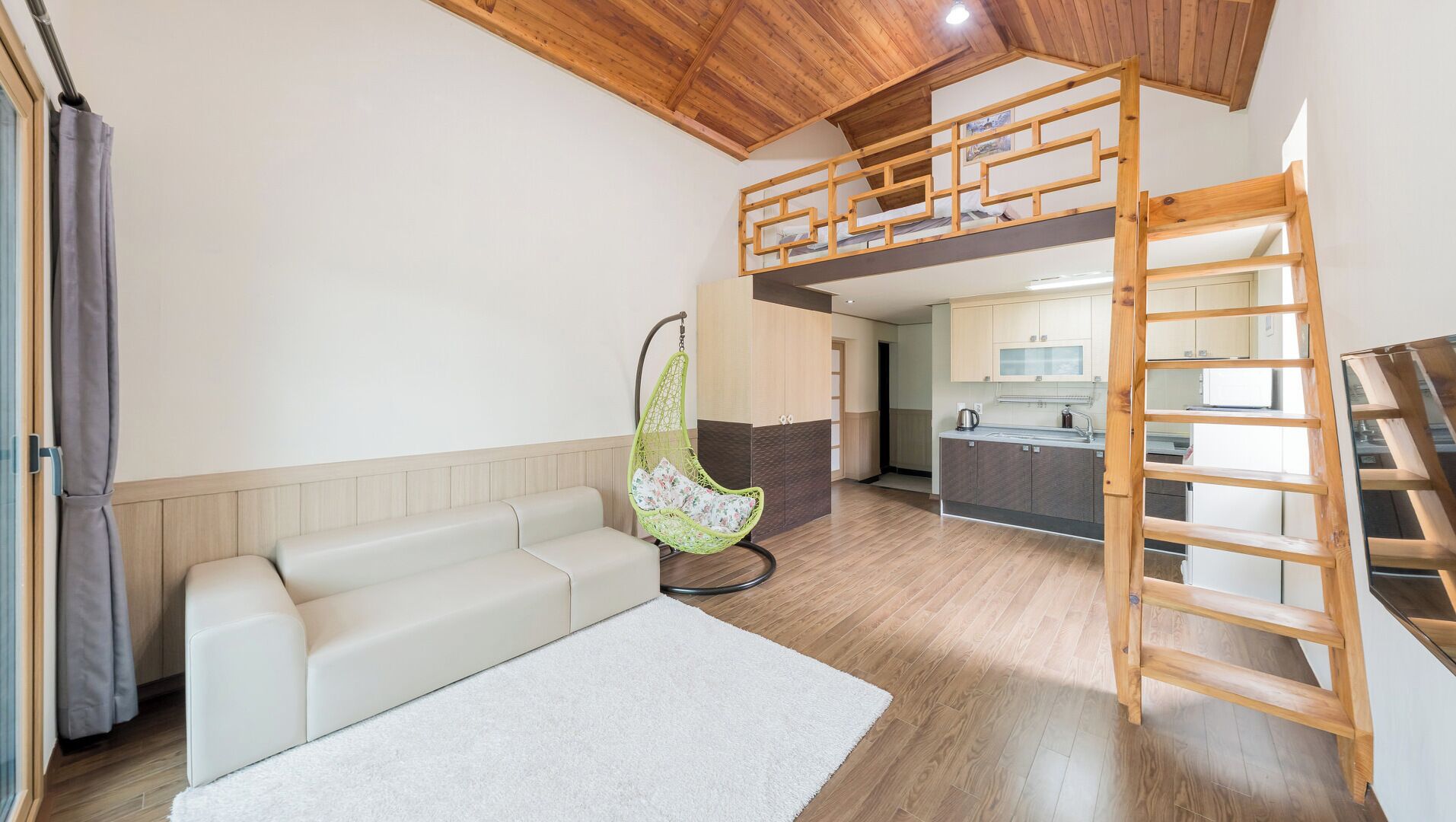 A loft-style room with a bunk bed, a hanging chair, a sofa, and a kitchen area.