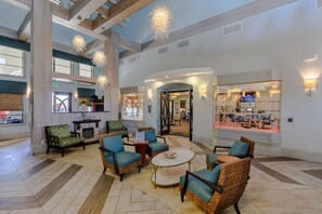 Eine geräumige Lobby mit hohen Decken, großen Fenstern und einer zentralen Sitzecke mit Korbstühlen und einem Couchtisch.