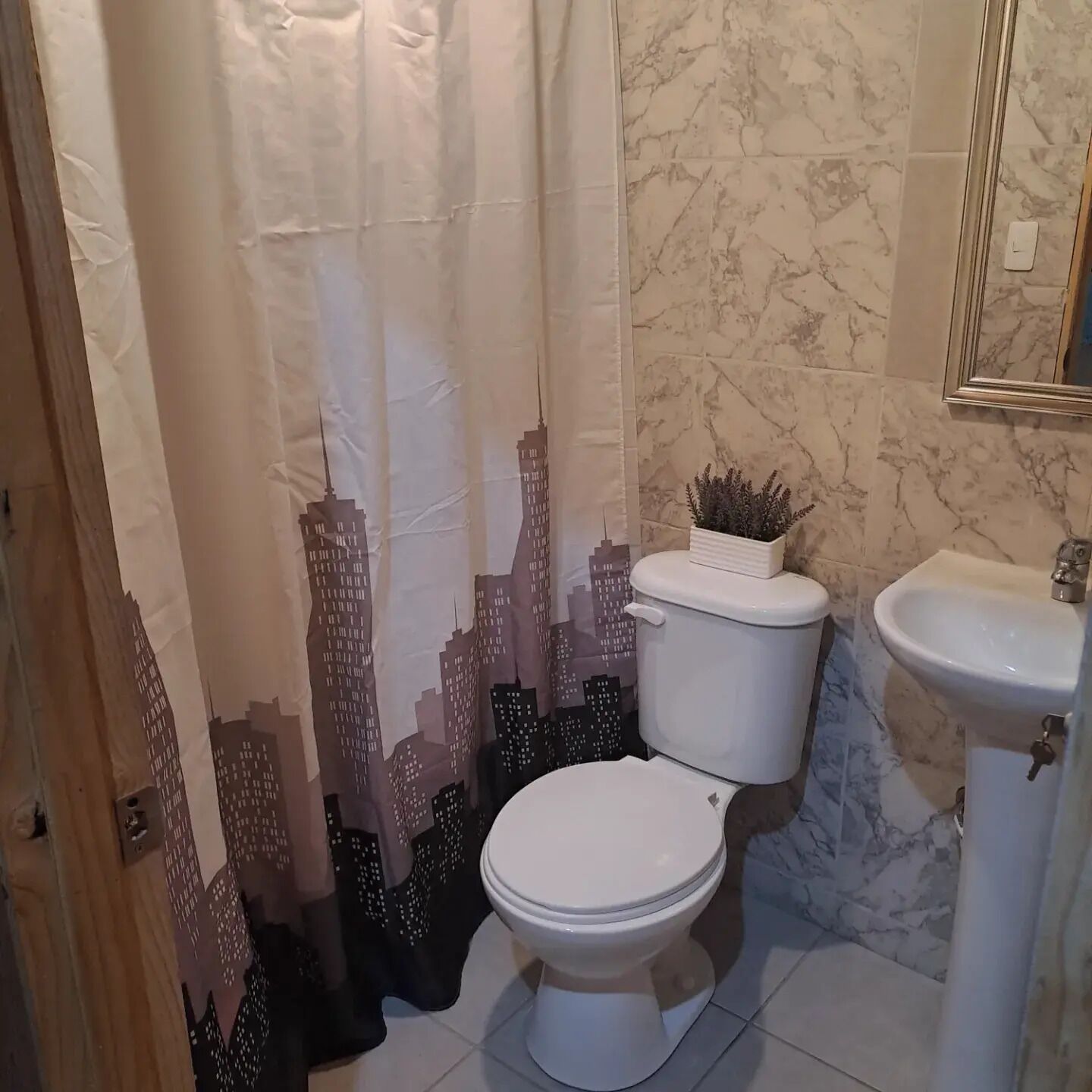 Ein Badezimmer mit Toilette, Waschbecken und einer Duschkabine mit Stadtblick-Motiv.