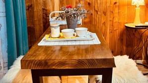 A wooden dining table with a placemat, a vase with dried flowers, and a lamp on a side table. - Cabins in Pucon (Araucanía)