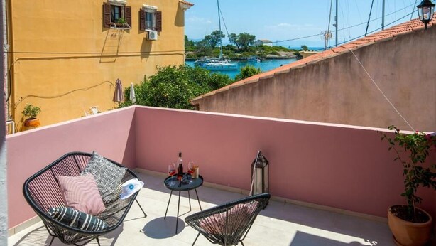 A balcony with two chairs, a small table with drinks, and a view of boats and buildings.