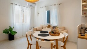 A modern living room with a round dining table, white chairs, a sofa, and a hanging light fixture.