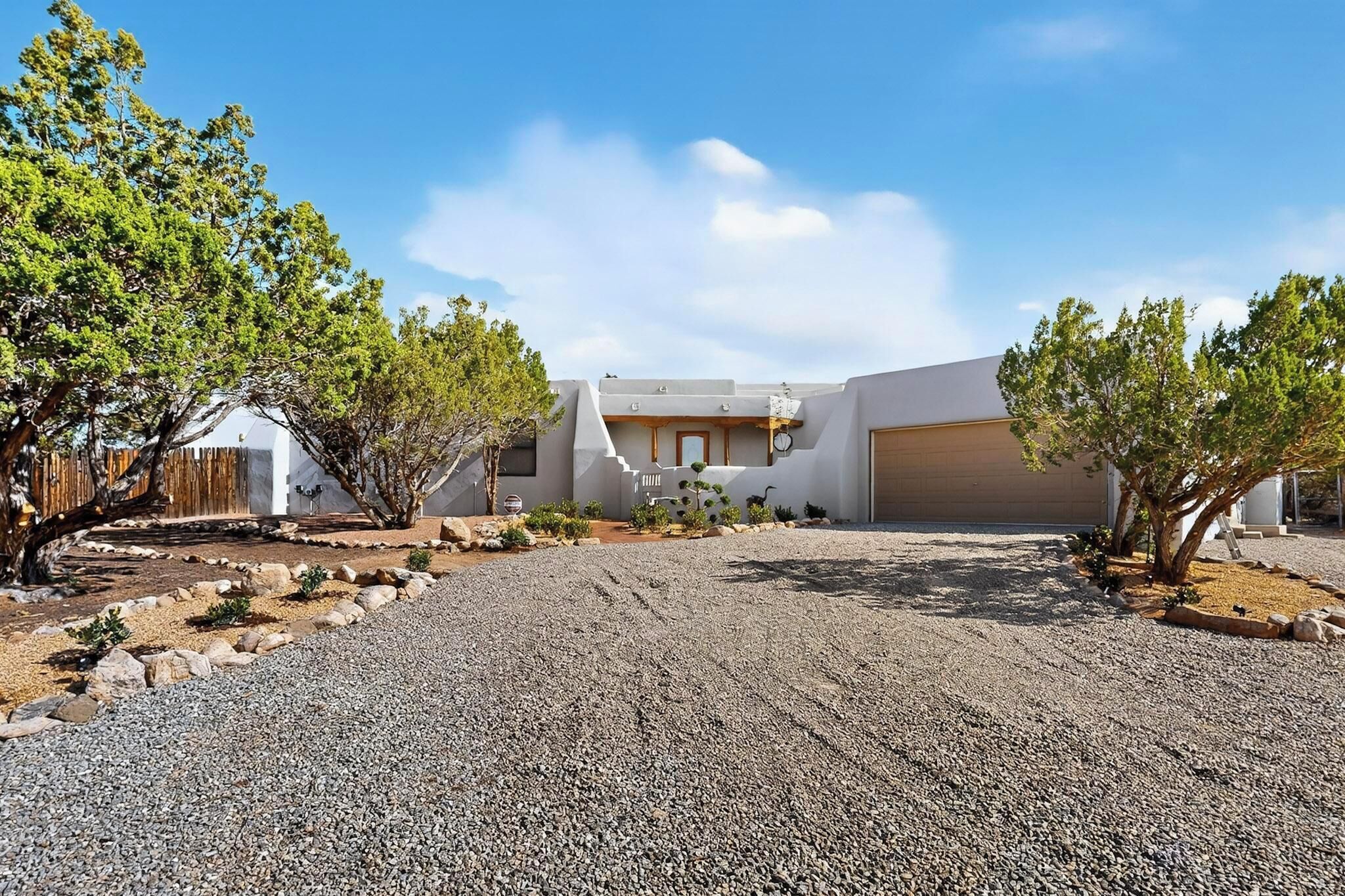 A modern building with a gravel driveway, surrounded by trees and a clear sky.