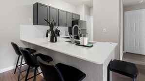A modern kitchen with a white countertop, dark cabinets, and a stainless steel sink. - Spacious 3-bedroom apartment - Close to Food and Fun! (Houston)