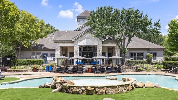 A pool area with lounge chairs and umbrellas, a stone building with a tower, and a clear sky. - Spacious 3-bedroom apartment - Close to Food and Fun! (Houston)