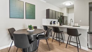 A modern kitchen with a dining area, featuring a round table, black chairs, and a white countertop. - Spacious 3-bedroom apartment - Close to Food and Fun! (Houston)