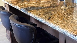Una cucina con piano in granito, elettrodomestici in acciaio inossidabile e sgabelli da bar neri.