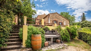 Un bâtiment en pierre avec un escalier menant à une terrasse en bois, le tout entouré de verdure.