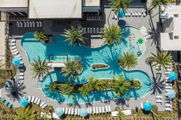 Vue aérienne d’un complexe hôtelier avec une grande piscine centrale, entourée de palmiers et de chaises longues.