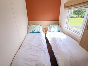 A double bed with white bedding and two matching pillows, a wooden headboard, and a window with a view of a grassy area. - Ewe View (Boston)