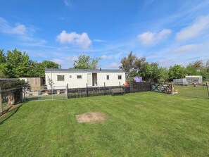 A mobile home with a fenced yard, a small shed, and a trailer in the background. - Ewe View (Boston)