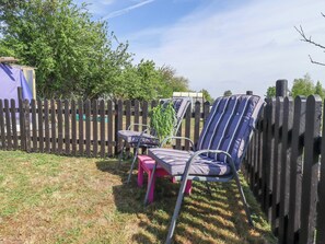 Un espace extérieur clos, avec deux chaises et une table, une clôture en bois et des arbres en arrière-plan.