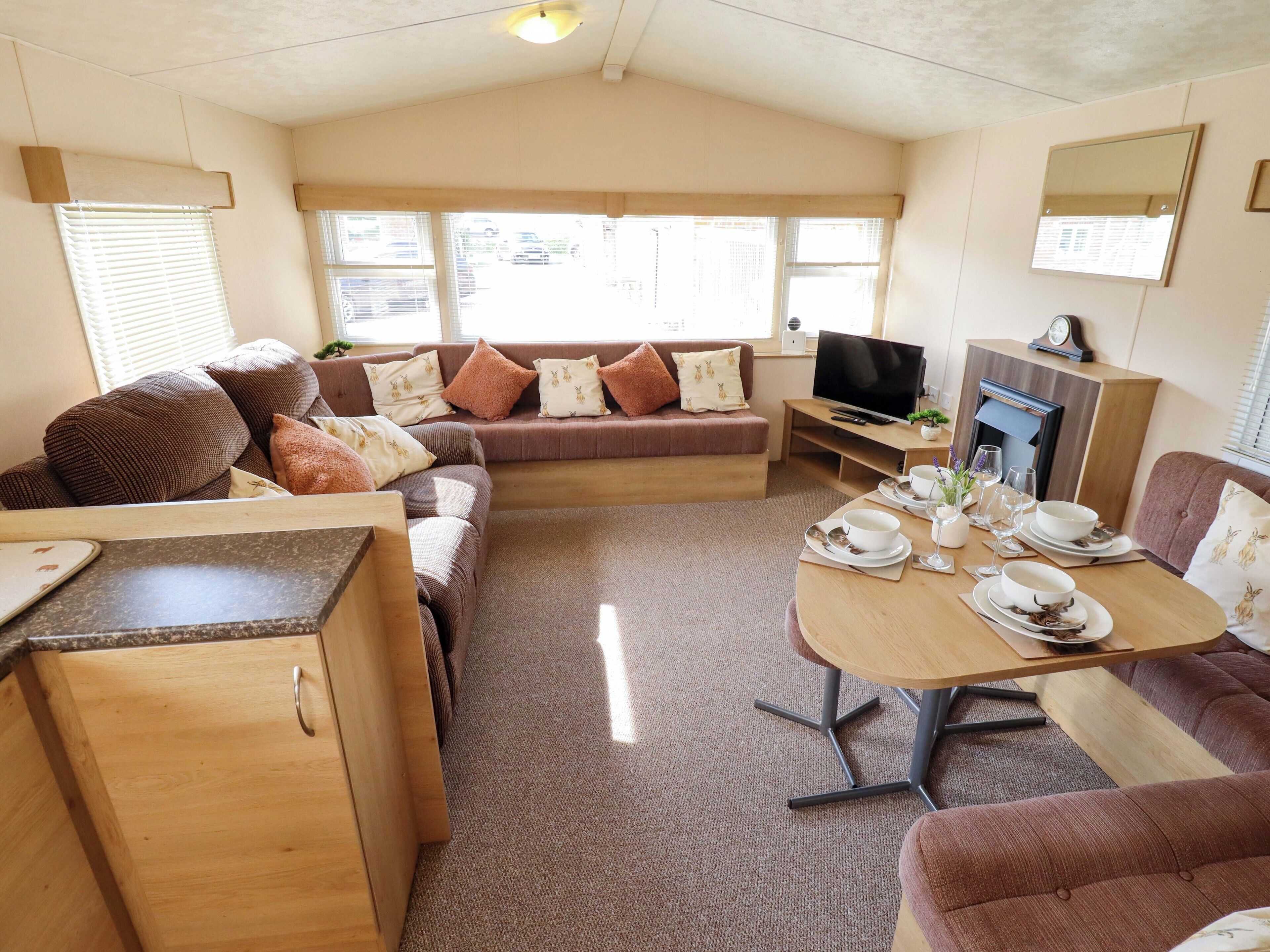 Interior acollidor d'una caravana amb sofà, taula de dinar, televisió i una petita cuina.