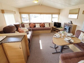 Un interior de autocaravana acogedor, con sofá, mesa de comedor, televisor y una pequeña cocina.