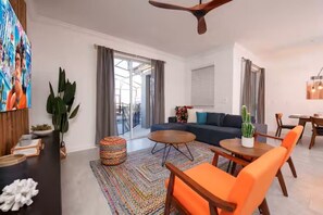Een moderne woonkamer met een bank, salontafel en stoelen, een eethoek met een tafel en stoelen, en een plafondventilator.