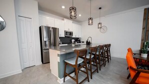Een moderne keuken met roestvrijstalen apparatuur, een centraal eiland en een eethoek met houten stoelen en een tafel.