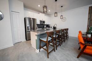 Een moderne keuken met roestvrijstalen apparatuur, een centraal eiland en een eethoek met houten stoelen en een tafel.