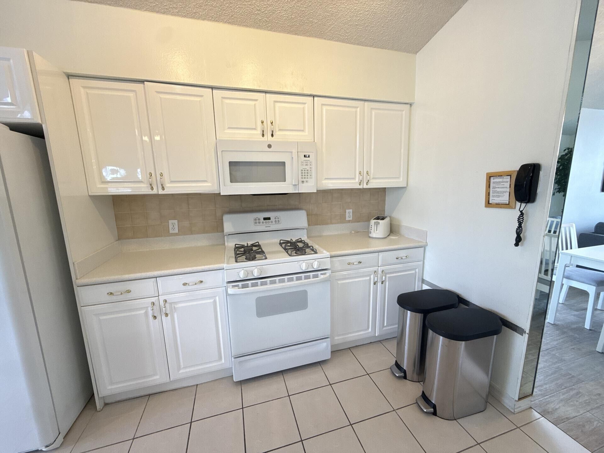 A compact kitchen with white cabinets, a microwave, a gas stove, and two stainless steel trash bins.