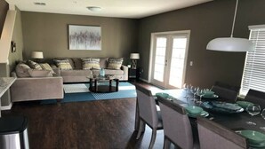 A living room with a sofa, coffee table, and dining area with chairs and a table set for a meal. - Last Minute Disney Getaway! Townhome with Themed Bedrooms. Book Now! #170005 (Orlando)