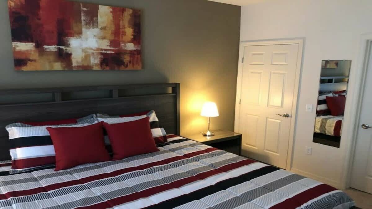Ein Hotelzimmer mit Bett, Nachttisch, Lampe, Tür und Spiegel.