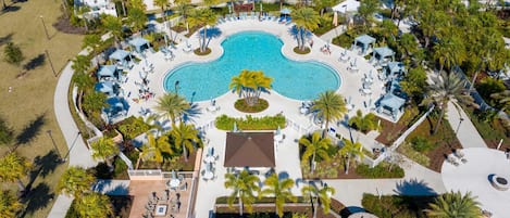An aerial view of a resort with a central swimming pool, surrounded by lounge areas and palm trees.