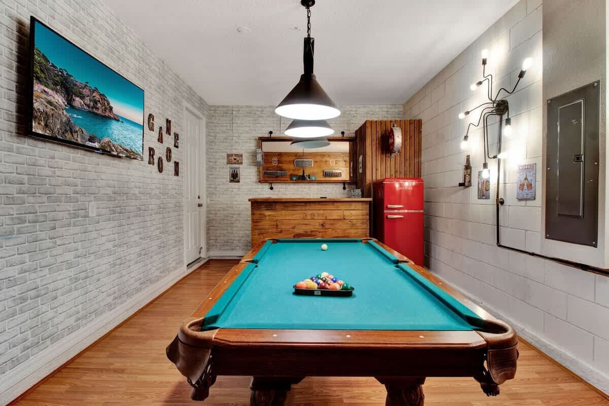 A pool table with balls, a wooden cabinet, a red refrigerator, and a wall-mounted TV.