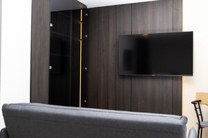 Una habitación moderna con un televisor de pantalla plana montado en una pared de madera oscura, un sofá gris y una silla de madera.
